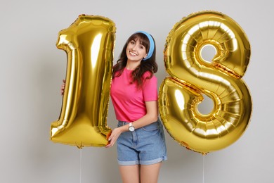 Coming of age party - 18th birthday. Young woman holding number shaped balloons on light grey background