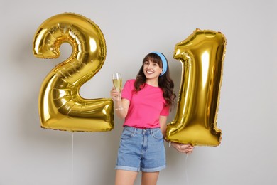 Photo of Coming of age party - 21st birthday. Young woman with glass of wine holding number shaped balloons on light grey background