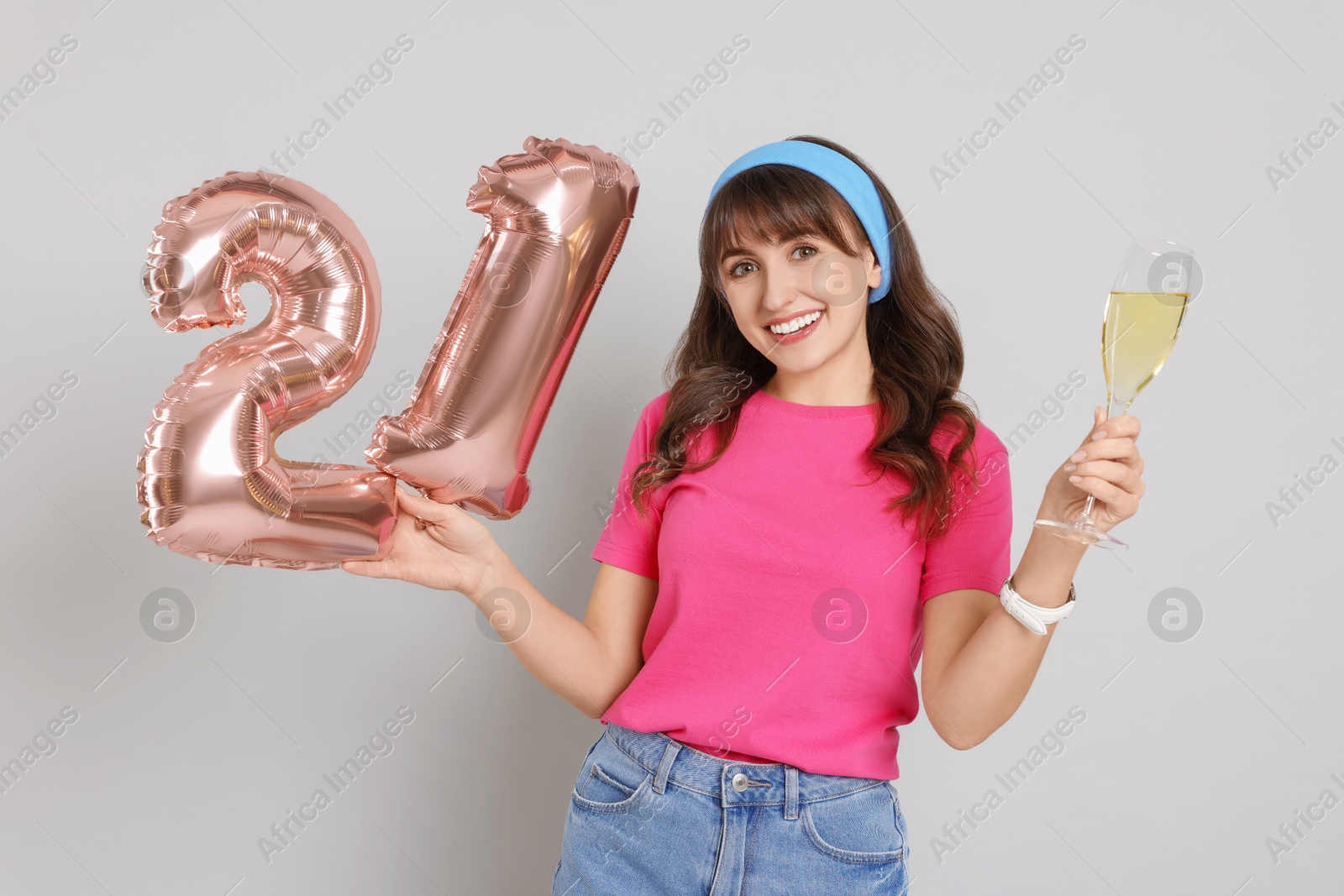 Photo of Coming of age party - 21st birthday. Young woman with glass of wine holding number shaped balloons on light grey background