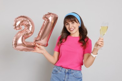 Photo of Coming of age party - 21st birthday. Young woman with glass of wine holding number shaped balloons on light grey background