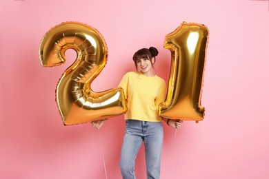 Photo of Coming of age party - 21st birthday. Young woman holding number shaped balloons on pink background