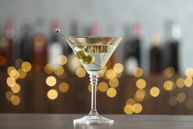 Photo of Martini cocktail with olives in glass on wooden table against blurred background. Bokeh effect