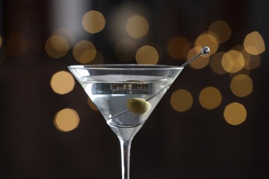 Photo of Martini cocktail with olive in glass on blurred background, closeup. Bokeh effect