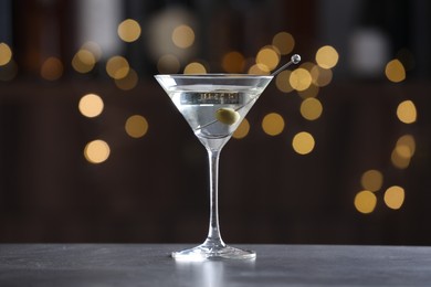 Photo of Martini cocktail with olive in glass on grey table against blurred background. Bokeh effect