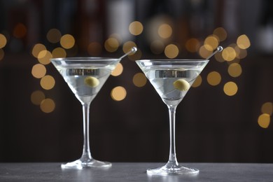 Martini cocktail with olives in glasses on grey table against blurred background. Bokeh effect