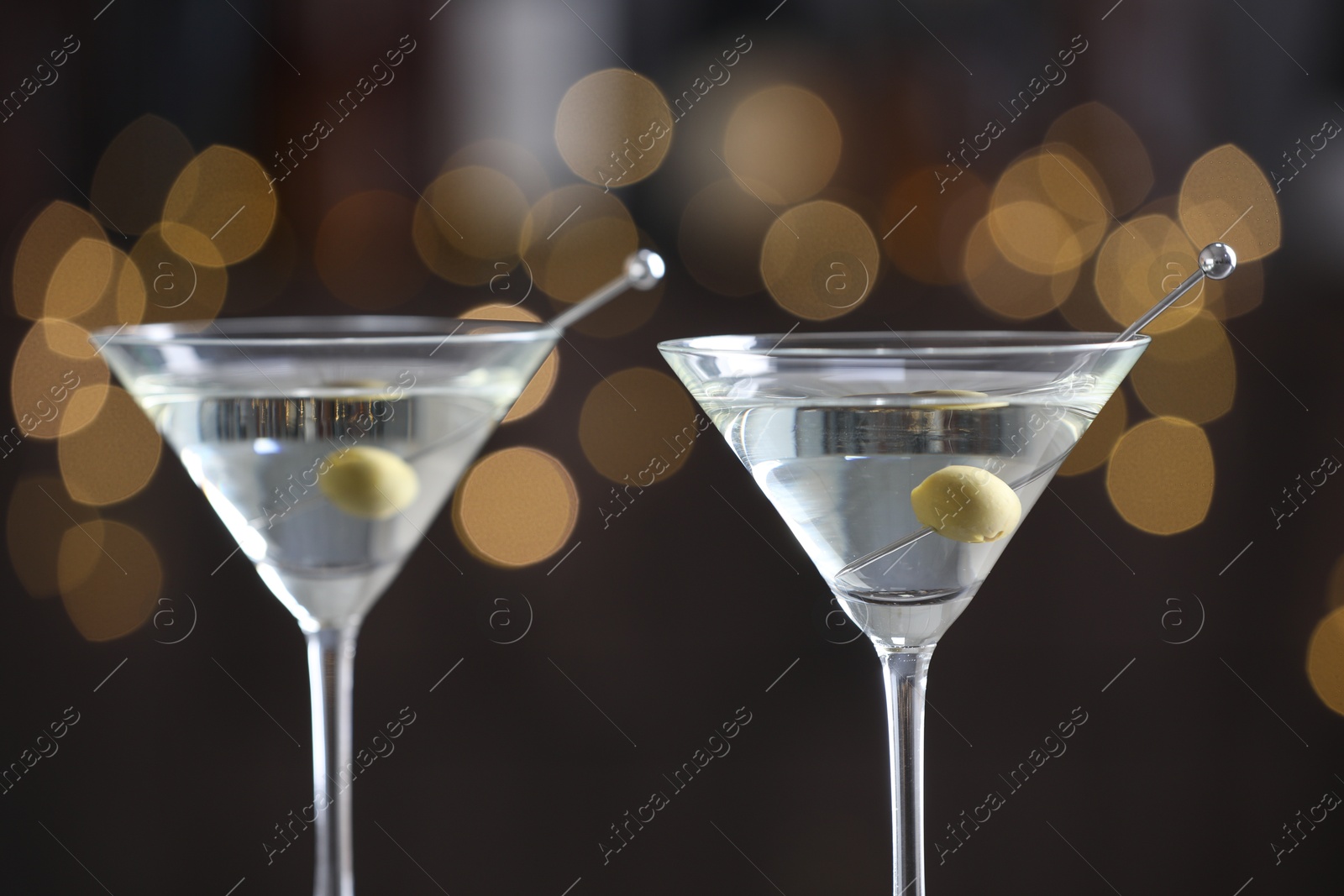 Photo of Martini cocktail with olives in glasses on blurred background, closeup. Bokeh effect