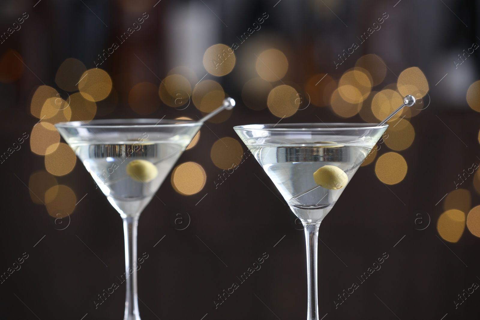 Photo of Martini cocktail with olives in glasses on blurred background, closeup. Bokeh effect