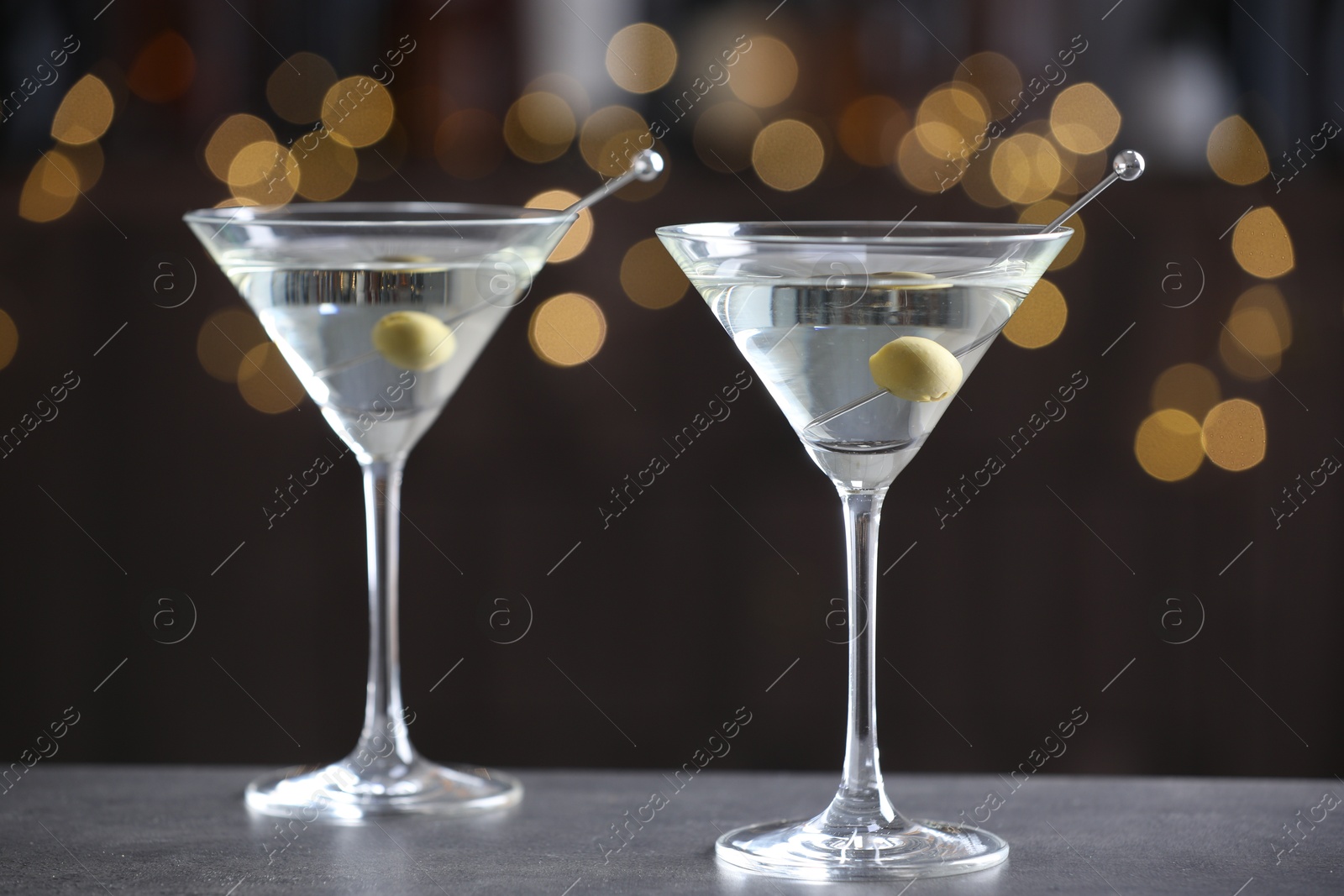 Photo of Martini cocktail with olives in glasses on grey table against blurred background, closeup. Bokeh effect