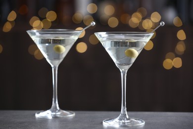 Martini cocktail with olives in glasses on grey table against blurred background, closeup. Bokeh effect