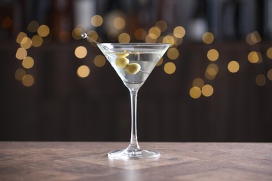 Photo of Martini cocktail with olives in glass on wooden table against blurred background. Bokeh effect