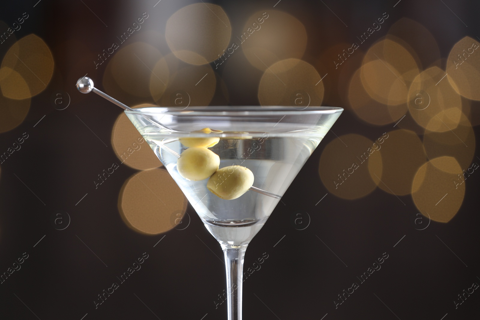 Photo of Martini cocktail with olives in glass on blurred background, closeup. Bokeh effect