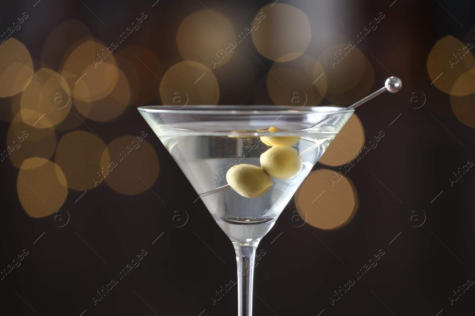 Photo of Martini cocktail with olives in glass on blurred background, closeup. Bokeh effect