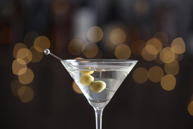 Photo of Martini cocktail with olives in glass on blurred background, closeup. Bokeh effect