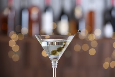 Photo of Martini cocktail with olives in glass on blurred background, closeup. Bokeh effect