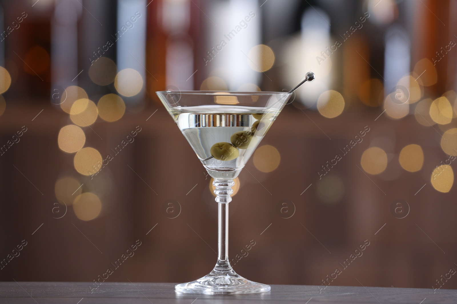 Photo of Martini cocktail with olives in glass on wooden table against blurred background. Bokeh effect