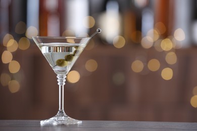 Photo of Martini cocktail with olives in glass on wooden table against blurred background. Bokeh effect