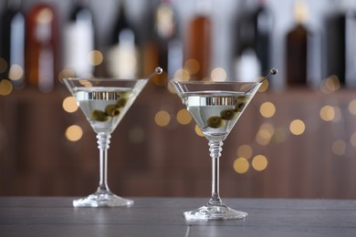 Photo of Martini cocktail with olives in glasses on wooden table against blurred background. Bokeh effect