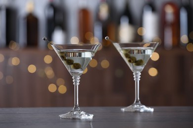 Photo of Martini cocktail with olives in glasses on wooden table against blurred background. Bokeh effect