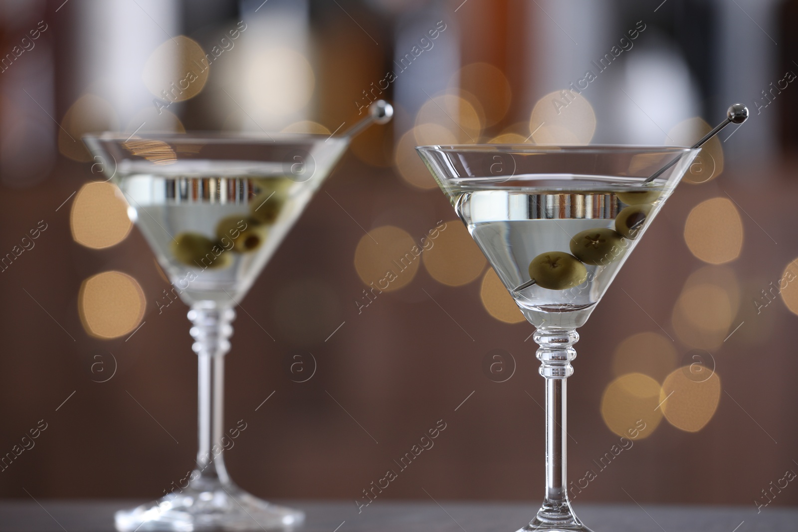 Photo of Martini cocktail with olives in glasses on wooden table against blurred background, closeup. Bokeh effect