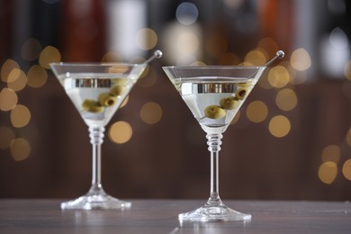 Photo of Martini cocktail with olives in glasses on wooden table against blurred background. Bokeh effect