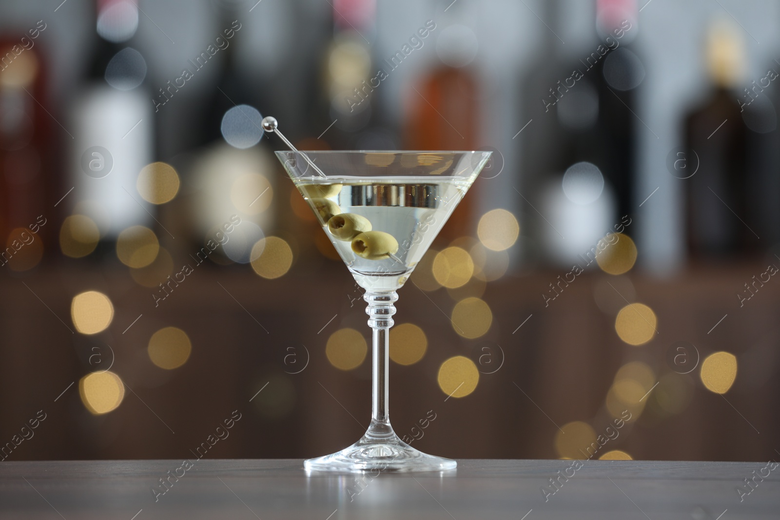 Photo of Martini cocktail with olives in glass on wooden table against blurred background. Bokeh effect