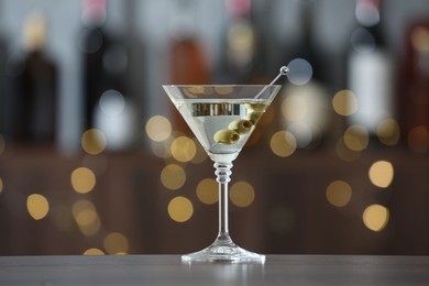 Photo of Martini cocktail with olives in glass on wooden table against blurred background. Bokeh effect