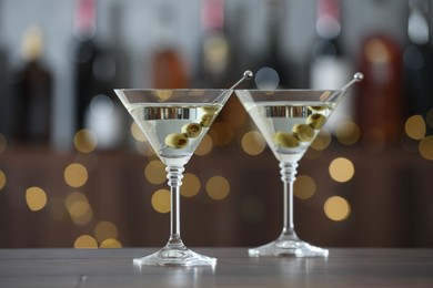 Photo of Martini cocktail with olives in glasses on wooden table against blurred background. Bokeh effect