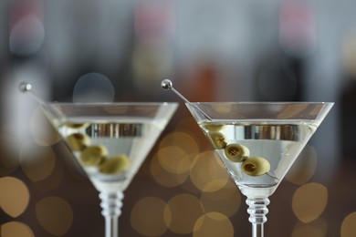 Photo of Martini cocktail with olives in glasses on blurred background, closeup. Bokeh effect