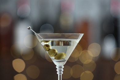 Photo of Martini cocktail with olives in glass on blurred background, closeup. Bokeh effect