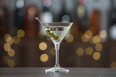 Martini cocktail with olives in glass on wooden table against blurred background. Bokeh effect