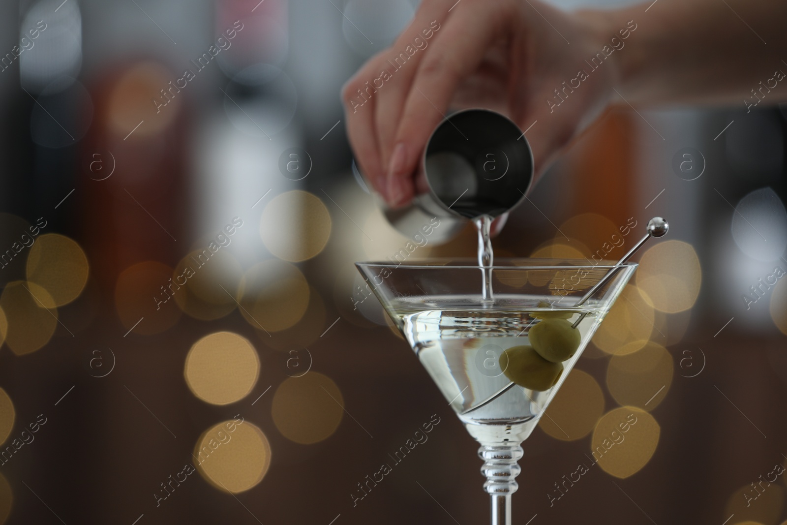 Photo of Woman making tasty martini cocktail with olives on blurred background, closeup. Bokeh effect