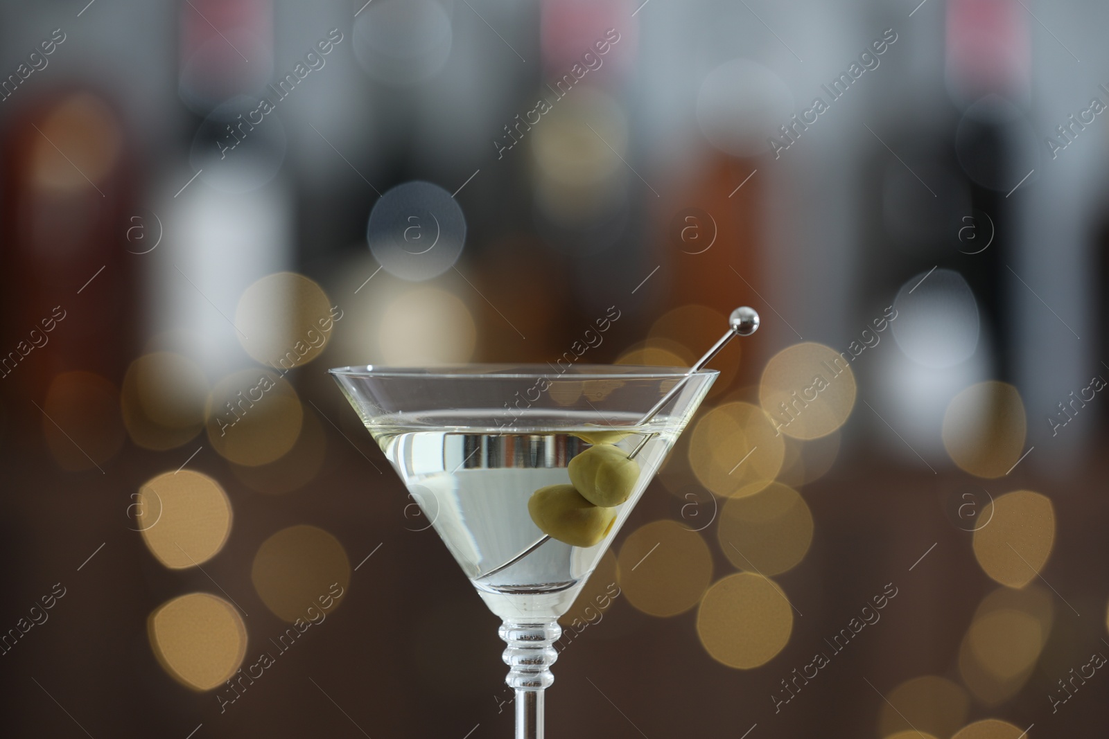 Photo of Martini cocktail with olives in glass on blurred background, closeup. Bokeh effect