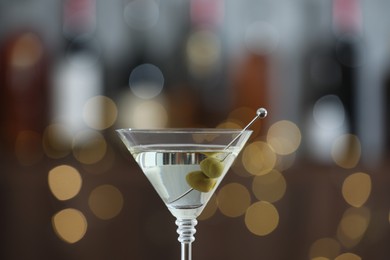 Photo of Martini cocktail with olives in glass on blurred background, closeup. Bokeh effect