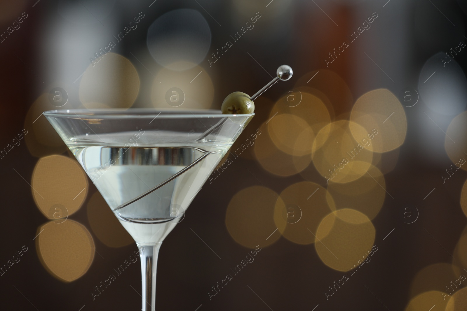 Photo of Martini cocktail with olive in glass on blurred background, closeup. Bokeh effect