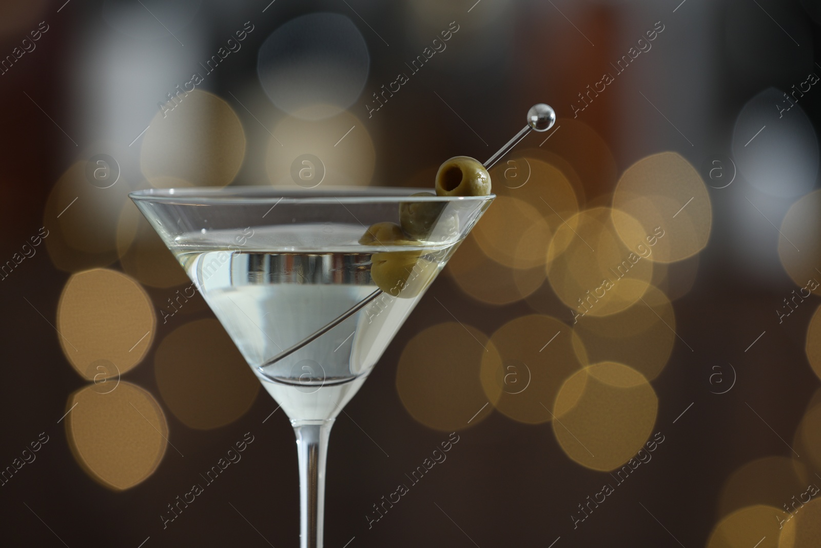 Photo of Martini cocktail with olive in glass on blurred background, closeup. Bokeh effect