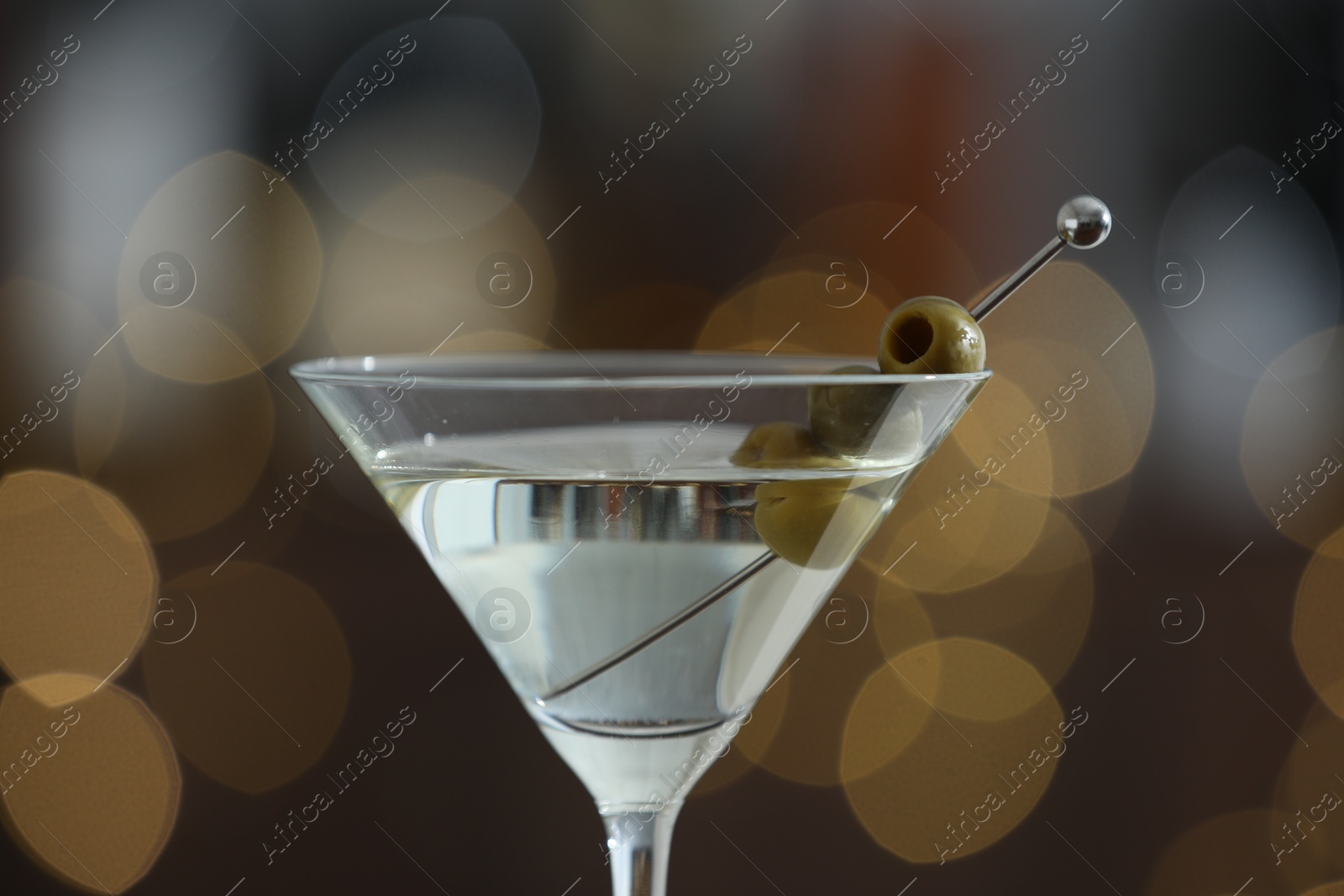 Photo of Martini cocktail with olives in glass on blurred background, closeup. Bokeh effect