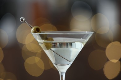 Photo of Martini cocktail with olives in glass on blurred background, closeup. Bokeh effect