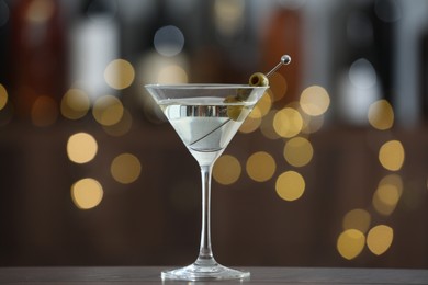 Photo of Martini cocktail with olives in glass on wooden table against blurred background. Bokeh effect