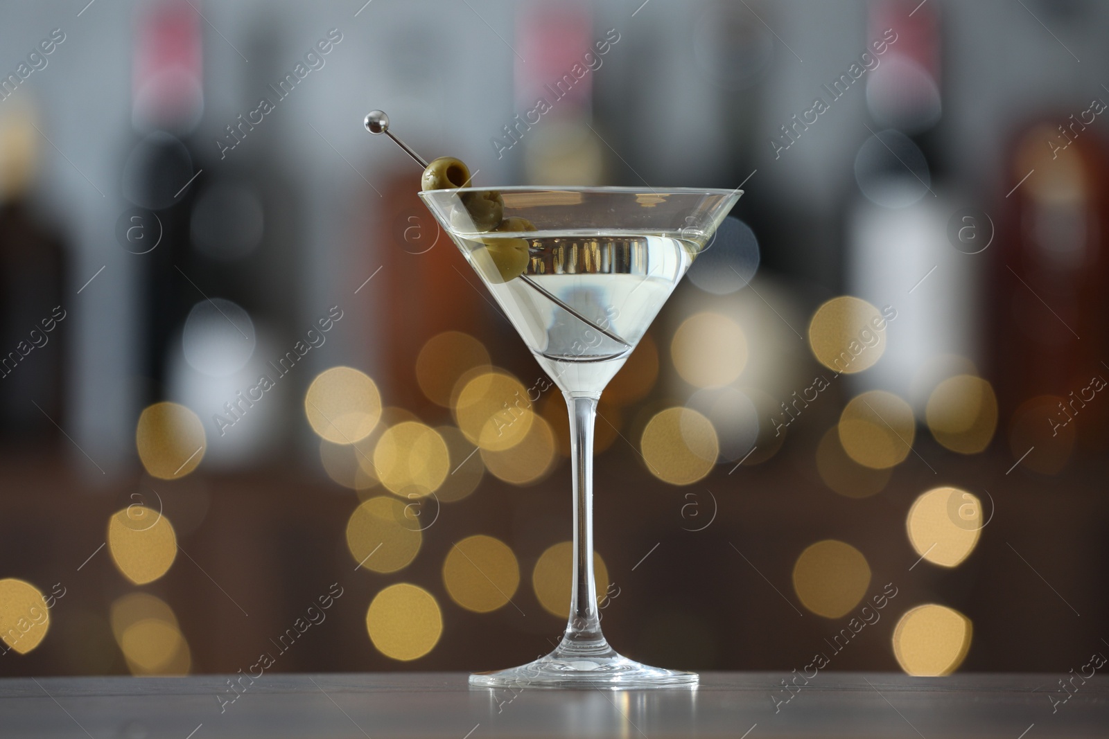 Photo of Martini cocktail with olives in glass on wooden table against blurred background. Bokeh effect