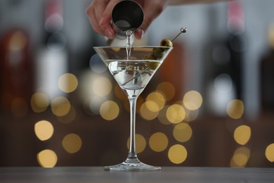 Photo of Woman making tasty martini cocktail with olives at wooden table on blurred background, closeup. Bokeh effect