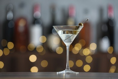 Photo of Martini cocktail with olives in glass on wooden table against blurred background. Bokeh effect