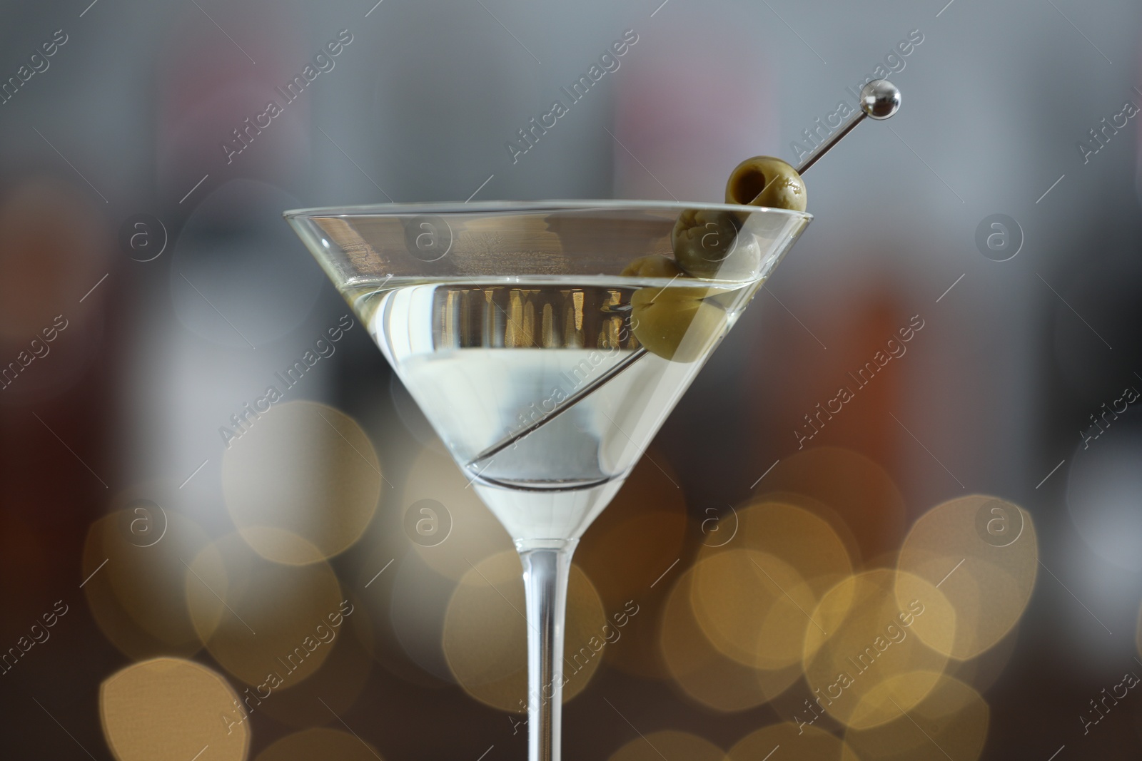 Photo of Martini cocktail with olives in glass on blurred background, closeup. Bokeh effect