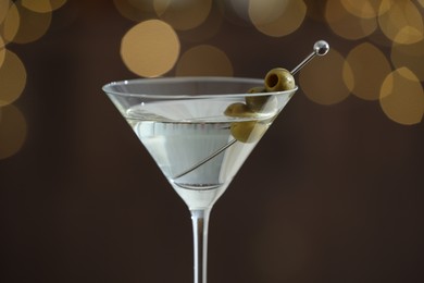 Photo of Martini cocktail with olives in glass on blurred background, closeup. Bokeh effect