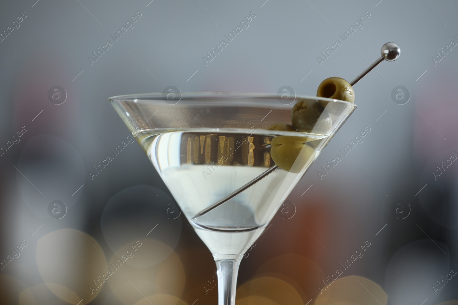 Photo of Martini cocktail with olives in glass on blurred background, closeup. Bokeh effect