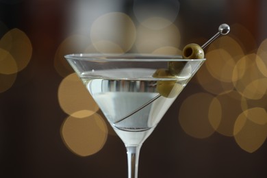 Photo of Martini cocktail with olives in glass on blurred background, closeup. Bokeh effect