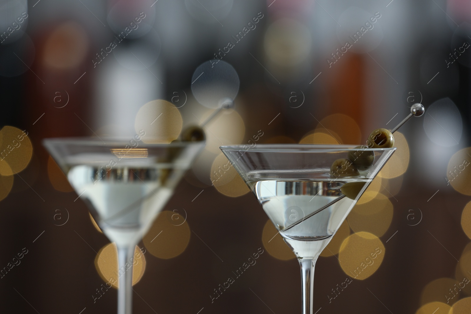 Photo of Martini cocktail with olives in glasses on blurred background, closeup. Bokeh effect