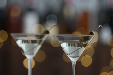 Photo of Martini cocktail with olives in glasses on blurred background, closeup. Bokeh effect