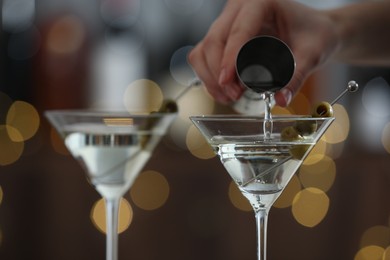 Photo of Woman making tasty martini cocktail with olives on blurred background, closeup. Bokeh effect