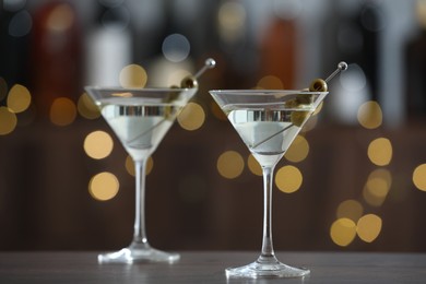 Photo of Martini cocktail with olives in glasses on wooden table against blurred background. Bokeh effect