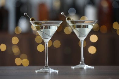 Photo of Martini cocktail with olives in glasses on wooden table against blurred background. Bokeh effect